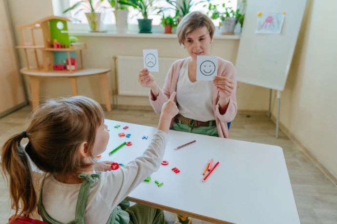 Child choosing the positive smile face that is being held up by the teacher